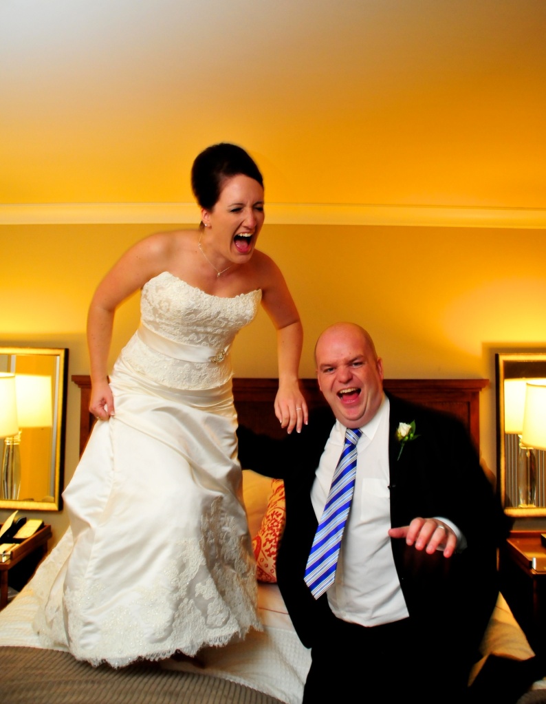 a couple jumping on the bed on their wedding day